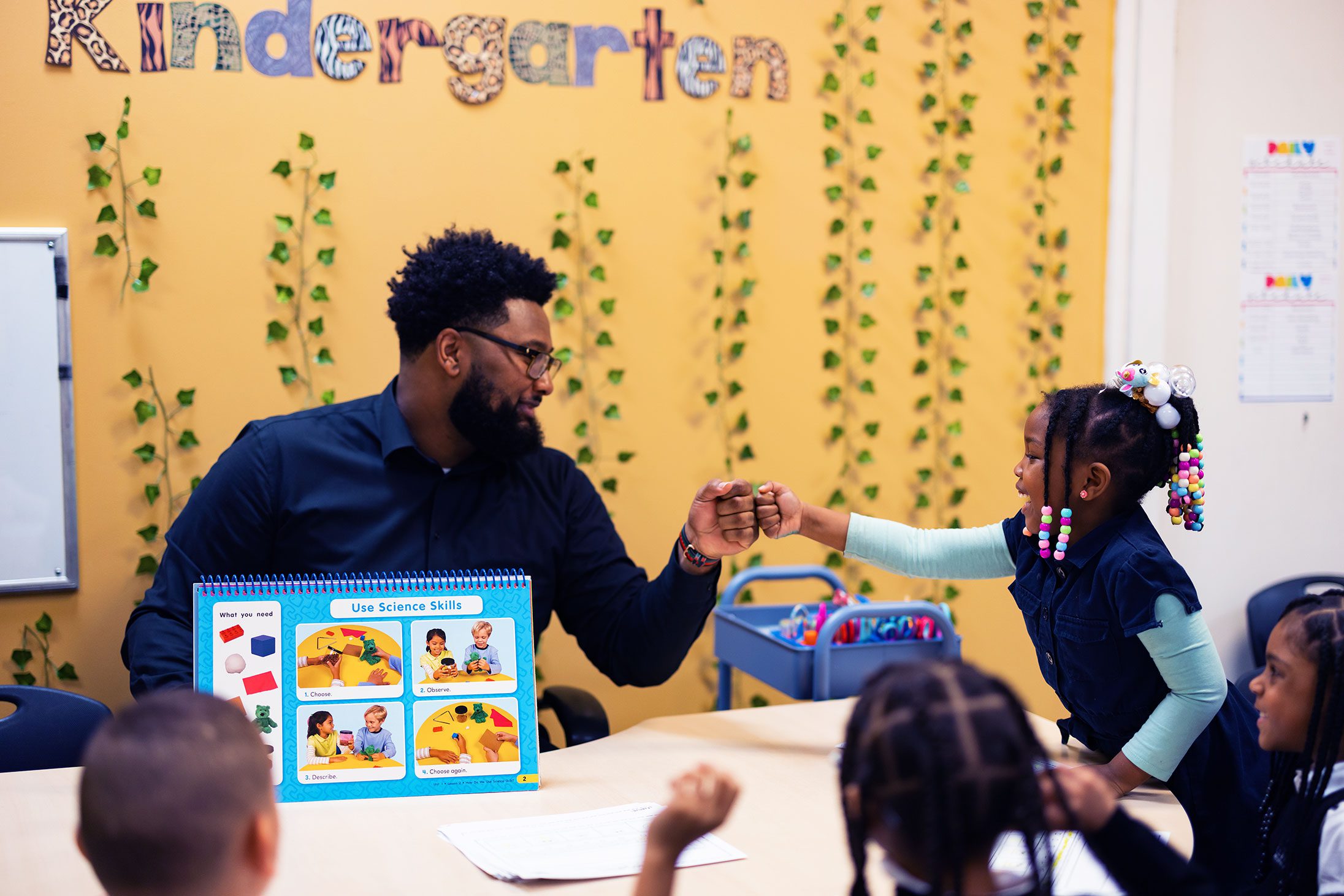 Smiling teacher and student fist bump in a classroom.