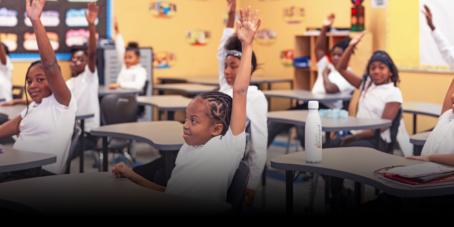 Smiling students with their hands up in class
